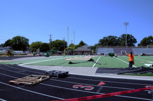 Workers lay artificial turf at the high school football stadium in preparation for the new season.
